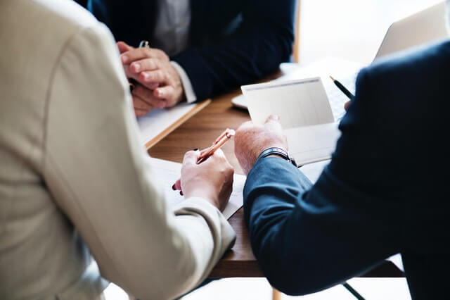 3 Banker sitzen am Tisch und unterzeichnen einen Vertrag